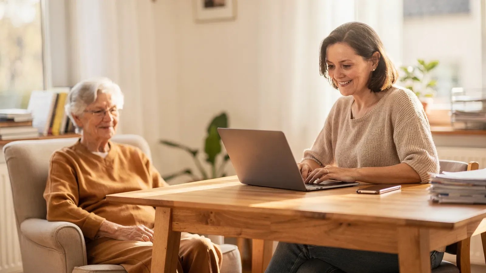 Angehoerige verbindet Arbeit am Laptop mit der Pflege eines aelteren Elternteils zuhause